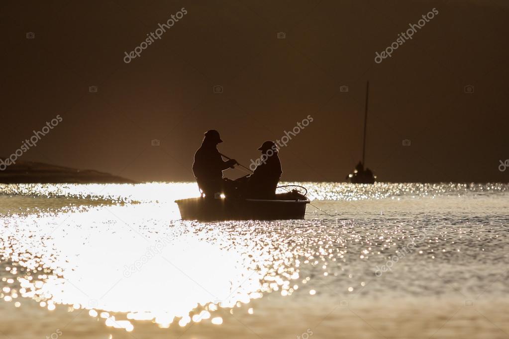 A boat on the water at sunset with two anglers against the light