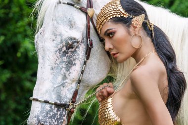 Seksi genç kadın vücudu ince, moda elf fantazisi giyiyor ve beyaz at arka planda..