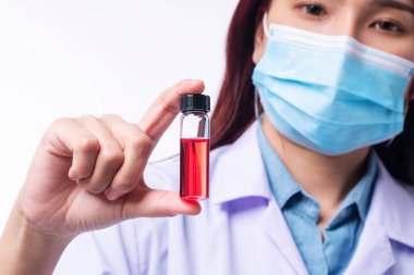 Genç kadın doktorun eli, izole edilmiş beyaz arka plan üzerinde kan örneğiyle test tüpü tutarken üniformalı beyaz elbiseler ve tıbbi maske virüsü virüsünü burnuna takıyor. Odaklanmayı seç