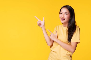 Neşeli genç kadın, sarı arka planda izole bir şekilde dikilirken ürünü veya boş kopya alanını işaret ederek parmak kullanıyor.