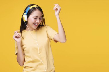 Hobi konsepti olan yaşam tarzı eğlencesi. Neşeli, kulaklık takan, müzik dinleyen, akıllı telefon çalan ve dans eden genç bir kadın. İzole edilmiş sarı arka planda rahatlıyor.. 