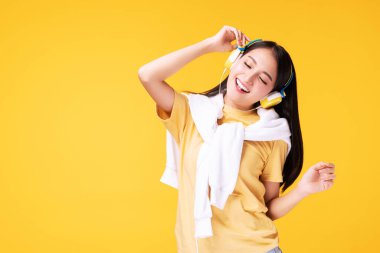 Hobi konsepti olan yaşam tarzı eğlencesi. Neşeli, kulaklık takan, müzik dinleyen, akıllı telefon çalan ve dans eden genç bir kadın. İzole edilmiş sarı arka planda rahatlıyor..
