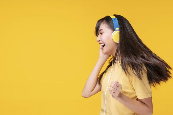趣味の概念を持つライフスタイルレジャー 陽気音楽フォームスマートフォンを聞いてヘッドフォンを身に着けている若い女性を楽しみ 孤立した黄色の背景の上にリラックスダンス — ストック写真