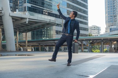 Evrak çantası taşıyan genç bir işadamı bacağını mutlu bir şekilde kaldırıyor..