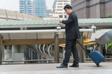 Orta yaşlı işadamı valizini modern şehirde gezdiriyor. Boşluğu kopyala