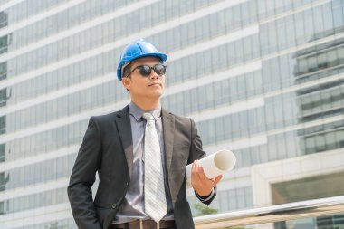 Yakışıklı Asyalı genç mühendis modern şehirde mavi baskı tutuyor..