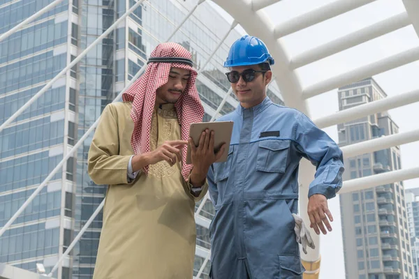 阿拉伯商人为一个年轻工程师持有平板电脑查看项目 — 图库照片