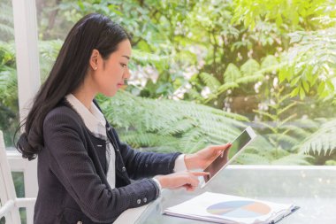 İş kadını bahçenin yanındaki oturma odasında tablete bakıyor..