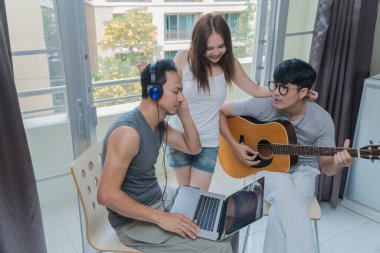 Bir grup arkadaş müzik için şarkı söylerken kulaklık ve dizüstü bilgisayar kullanıyorlar ve odada mutlu bir şekilde gitar çalıyorlar.. 