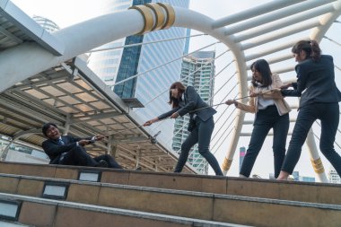 Üç iş kadını ve orta yaşlı işadamları halat çekme oyunu oynuyorlar.