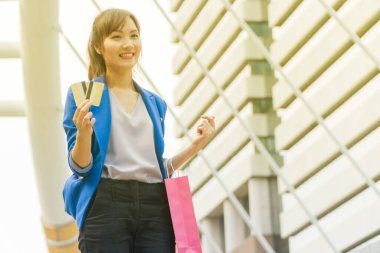 Güzel bir kadın elinde iki kredi kartı, kollarında bir alışveriş çantasıyla ayakta duruyor..