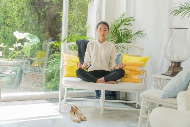 Güzel kadın oturma odasında yanında bir yığın renkli kitapla uzun beyaz bir sandalyede meditasyon yapıyor. Boş zaman konsepti