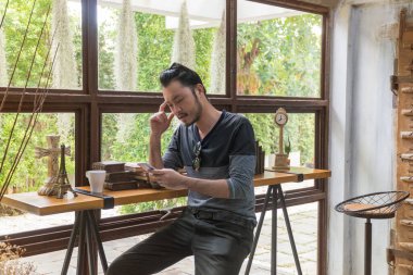 Asyalı yakışıklı adam yüksek sandalyedeki akıllı telefonları izliyor..