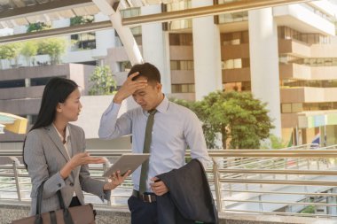 İki Asyalı İş Adamının Sorunu ve Başarısızlığı, Tabletlerle Tartışan Erkek ve Kadın. Genç iş adamları başlarını tutup yaptıkları işten dolayı kendilerini kötü hissediyorlar..