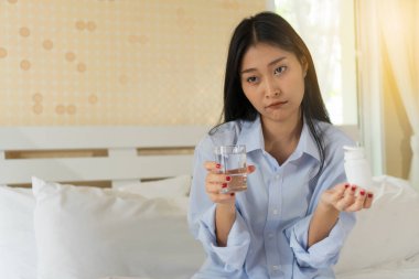 Genç bir kadın ilaç almaktan sıkılıyor. Yatağında bir şişe ilaç ve bir bardak su tutan güzel genç bir kadın ilaç almak istemiyor..