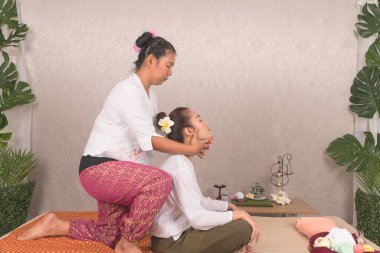 Thai masajını kabul et. Güzel Asyalı genç kadın spa salonundaki bitkisel masaj yaptırıyor. Taylandlı kız refleksolojisi masörle omuz omuza..