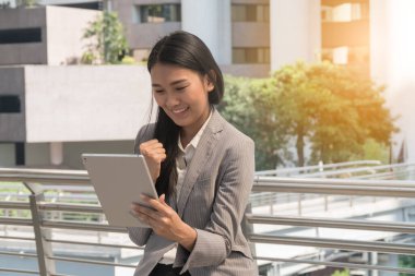 Tableti tutan uzun saçlı genç bayanların başarısına sevinin. Modern şehirdeki iş kadını neşeli ve heyecanlı hissediyor. İş kadını işten sonra gri takım giyer. yaşam tarzı konsepti.