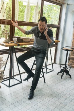 Kızgın Asyalı genç adam cep telefonuyla konuşuyor ve evde öfkeyle bağırıyor..