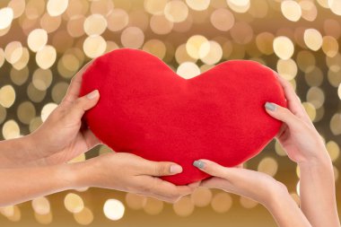 Soyut bokeh sarı ışıklarda kırmızı kalbi bir arada tutan iki el bulanık arka plana odaklandı. Sevgililer Günü konseptinde aşk ve romantizm.