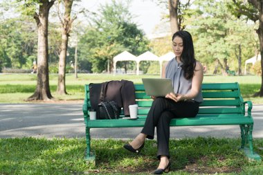 Orta yaşlı iş kadını parkta bankta otururken dizüstü bilgisayar kullanıyor. Rahat yaşam tarzı konsepti. 