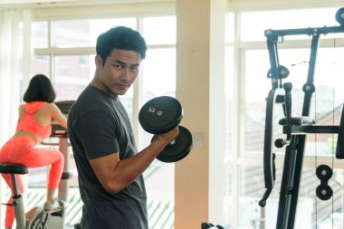 Spor salonunda dambılla oynayan yakışıklı adam. Vücut geliştirici adam spor salonunda halterle ağır ağırlık egzersizi yapıyor..