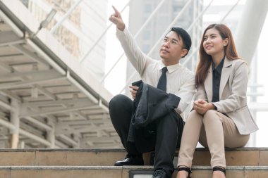İki iş adamı merdivenlerde oturmuş fotokopi alanı olan modern bir şehirde iş planından bahsediyorlar. İş adamı, iş kadınıyla gelecek arayışına işaret ediyor. Konsept planlama işi.