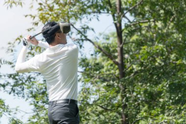 Beyaz tişörtlü, parıldayan golfçünün arkası. Genç adam golf sahasında vuruşunu çalışıyor..