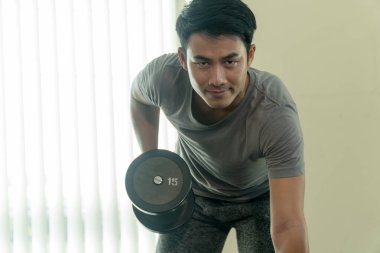 Spor salonunda dambılla oynayan yakışıklı adam. Vücut geliştirici adam spor salonunda halterle ağır ağırlık egzersizi yapıyor..