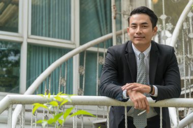 Yakışıklı genç adam merdivenlerde sigara tutarken takım elbise ve beyaz gömlek giyiyor. İşten sonra dinlenmek için dışarıda bekliyor..