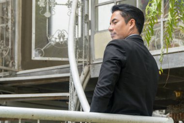 Yakışıklı genç adam merdivenlerde sigara içerken takım elbise ve beyaz gömlek giyiyor. İşten sonra dinlenmek için dışarıda bekliyor..