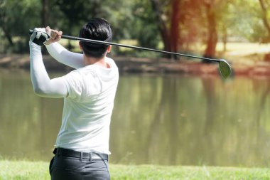 Beyaz tişörtlü, parıldayan golfçünün arkası. Genç adam golf sahasında vuruşunu çalışıyor..