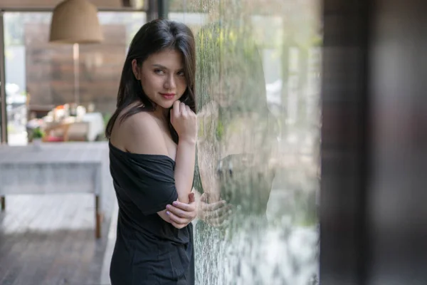 Young slim fit woman wearing back dress in front the mirror look at camera. Teenage girl wearing denim pants showing her beautiful fit body. Lifestyle and people concept