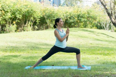 Parklarda yoga yapan orta yaşlı, beyaz bir kadın. Parktaki çimlerin üzerinde yoga minderi üzerinde duran kadın dışarıda egzersiz yapıyor. Sağlıklı yaşam tarzı kavramı.