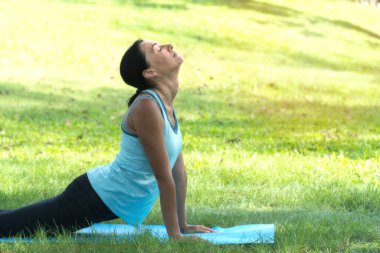 Parklarda yoga yapan orta yaşlı, beyaz bir kadın. Parktaki çimlerin üzerinde yoga minderi üzerinde duran kadın dışarıda egzersiz yapıyor. Sağlıklı yaşam tarzı kavramı.