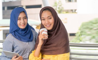 Arap kadınlar ellerinde fincanla sarı giyinmiş arkadaşlarıyla kahve içiyorlardı. Arap kadınlar tablet tutarak kameraya bakıyorlardı..