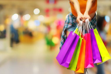 Alışveriş merkezlerinin arka planında renkli alışveriş torbaları tutan bir kadın. mutluluk, tüketim, satış ve insanlar konsepti.