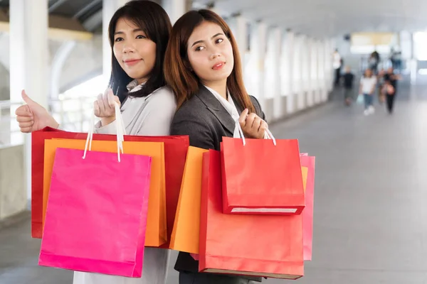 Happiness, consumer, sale and people concept. Attractive two young woman holding shopping bags looking at camera city street background with copy space.