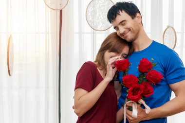 Odada genç bir çift var. Adam, kız arkadaşına sarılıyor ve oturma odasında gülümsüyor. Erkek arkadaşı olan güzel genç bir kadın ona arkadan sarılıyor..