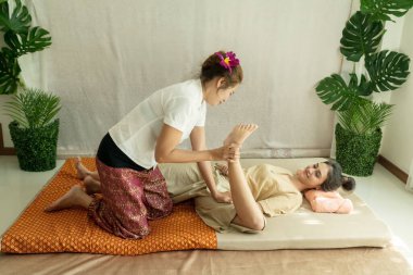 Thai masajını kabul et. Güzel Asyalı genç bir kadın spa salonunda bitkisel masaj yaptırıyor. Taylandlı kız masörle bacaklarını esnetiyor..