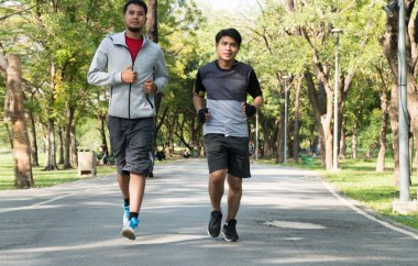 Farklı yaşlarda iki adam parkta birlikte koşuyor. İnsanlar doğa arka planında sağlığı korumak için dışarıda egzersiz yapıyorlar. Spor sağlıklı konsept.