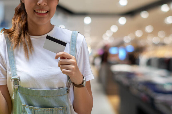 Attractive cheerful young woman holding credit card on shopping mall background. Lifestyle shopping concept.