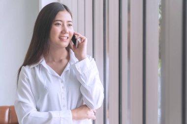 İş kadını akıllı telefon kenarından konuşur. Ofiste pencerenin kenarında duran çekici genç bir kadın. Dışarıya bakıyor ve telefonuyla konuşuyor..