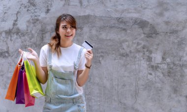 Neşeli genç bir kadın elinde bir sürü renkli alışveriş torbası ve arka planında fotokopi alanı olan beton duvarlarda boş bir kredi kartı tutuyor. mutluluk, tüketici, satış ve insanlar konsepti.