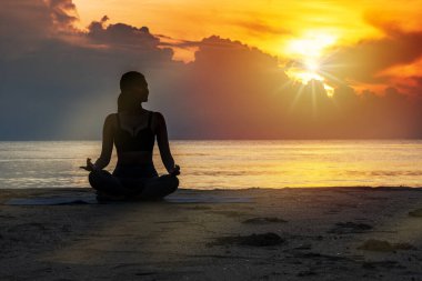 Sağlıklı konsept için meditasyon ve zen. Siluet genç kadın sabah güzel bir gündoğumuyla sahilde otururken yoga yapıyor..