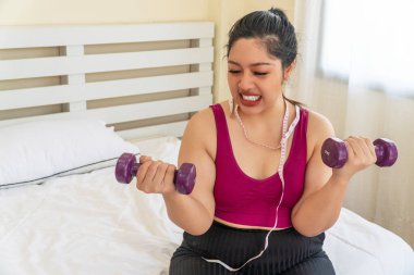 Tembel aktivite egzersizi diyet ya da obezite konsepti için uygun vücut. Ölçüm bandıyla boynunda halteri tutan yorgun şişman kadın yatakta otururken diyet yapıyor..
