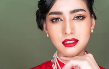 Kozmetik ya da Çin Yeni Yıl Kutlaması konsepti. Gri arka plandaki kameraya bakarken geleneksel kırmızı Cheongsam 'ı takan alımlı genç kadın saç stili. Kapat. 