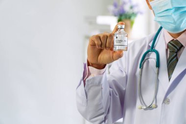 Coronavirus aşısı ya da koruyucu salgın konsepti. Doktor ya da bilim adamı üniforma giyer ve steteskopla tıbbi maske takar. Aşı test tüpünü ellerinde tutarlar..