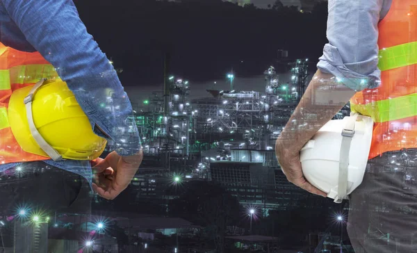 Teamwork concept. Two engineer man holding safety helmet hat protective in their hands while standing over petroleum oil background. Double exposure of engineer with oil refinery industry plant.