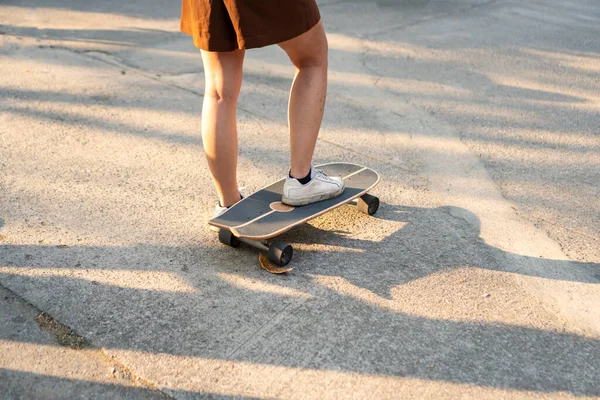 Aktivite eğlencesi kaykay tahtası yaşam tarzı konsepti. Sörf yapan atletik kadın bacakları. Akşamları güneş ışığı eşliğinde yolda kaykay yapıyor..