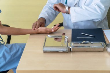 Sağlık hizmeti konsepti. Steteskop kullanan profesyonel bir doktorun eli, parmak kontrolü yapan nabız kontrol kolu kullanan, kol saati tutan bir hasta, klinikteki aletlerle birlikte masada oturuyor..